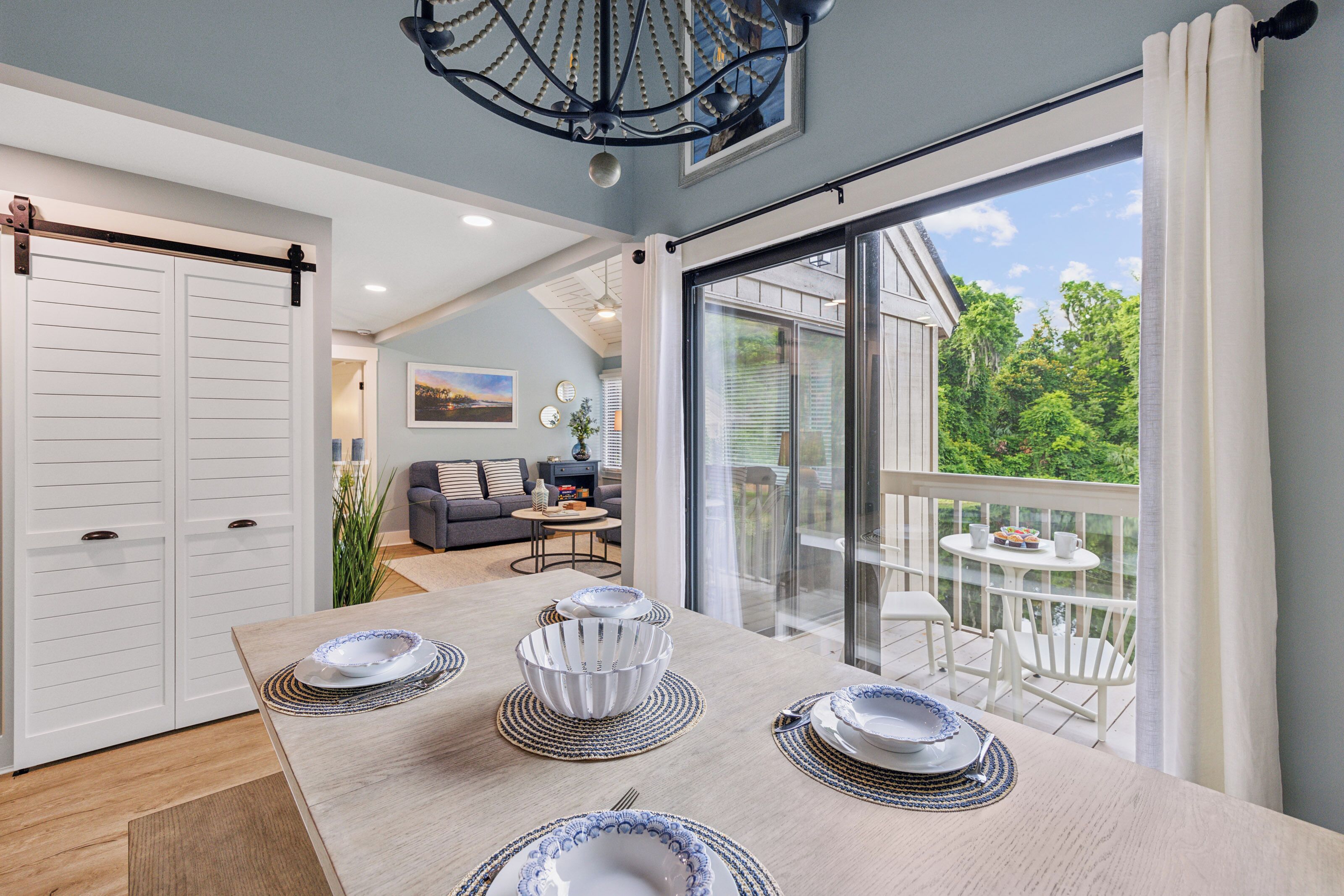 A dining area with a large table set for four, a sliding glass door leading to a balcony, and a cozy seating area with a sofa and coffee table.