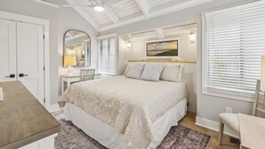 Un dormitorio con una cama grande, un escritorio, una silla, un espejo y una ventana con persianas.