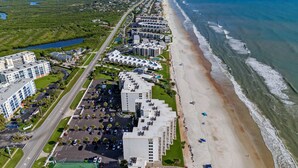 Vue aérienne d’un hôtel situé sur la côte, composé de plusieurs bâtiments, avec une plage et un court de tennis.