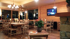 Ein Restaurant mit Holzvertäfelung, mehreren Tischen, Stühlen und einem an der Wand befestigten Fernseher.