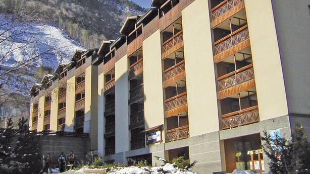 Ein mehrstöckiges Hotel mit Balkonen, einer Steinfassade und einer Bergkulisse.