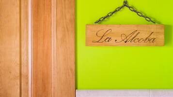 Un letrero de madera con 'La Alcoba' colgado en una pared verde brillante.