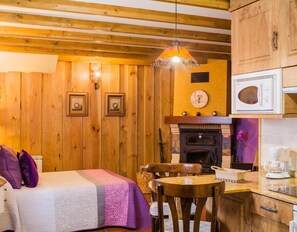 Una habitación acogedora con paredes de madera, una cama con manta colorida, una mesa de comedor con sillas, una chimenea y un microondas.