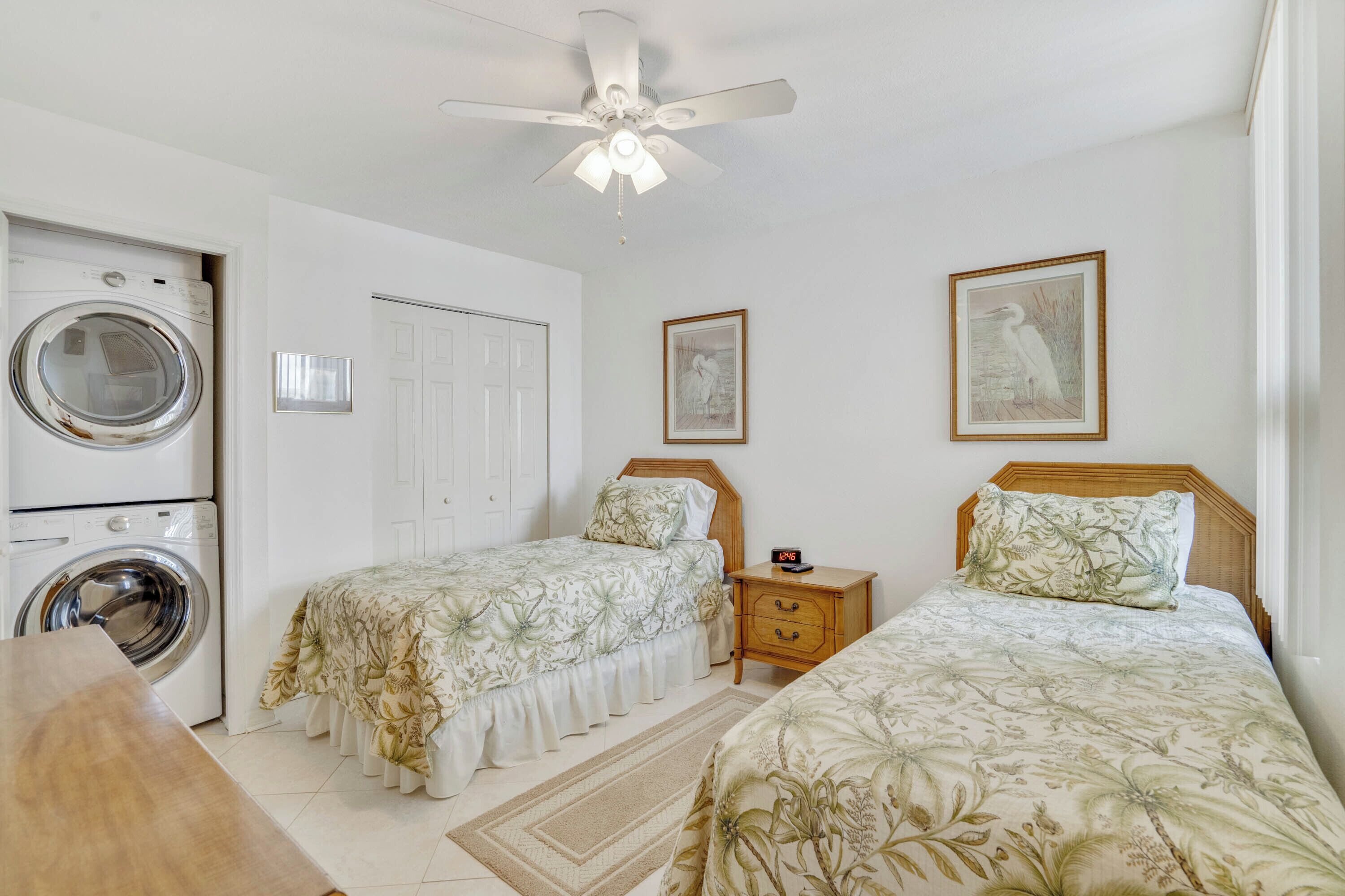 A bedroom with two beds, a washing machine, a ceiling fan, and two framed pictures on the wall.