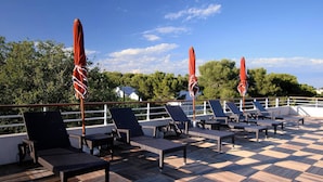A deck with lounge chairs and red umbrellas, overlooking a body of water and greenery. - Studio Climatisé Proche des Commerces (Antibes)