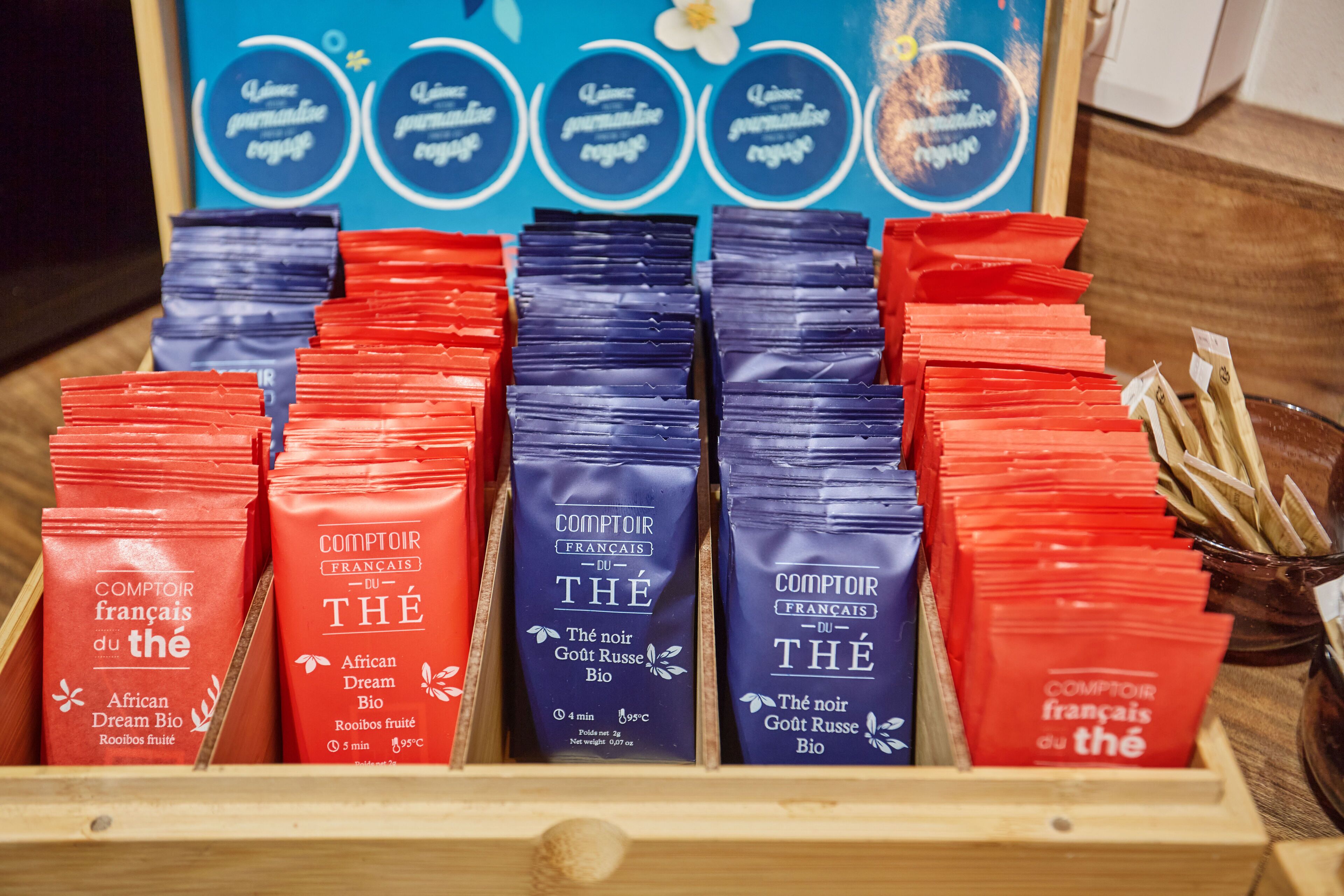 Una vitrina de madera con bolsas rojas y azules etiquetadas como "Comptoir français du Thé" y "African Dream Bio".