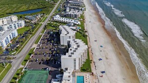 Vista aérea de un hotel costero con varias edificaciones, una playa y una cancha de tenis.
