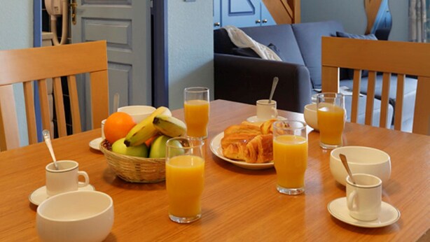 Una mesa de comedor con alimentos para el desayuno, una escalera y vista del salón.