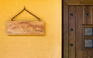 Une enseigne en bois représentant un paysage de montagne et portant l’inscription « La Devesa », fixée à un mur jaune.