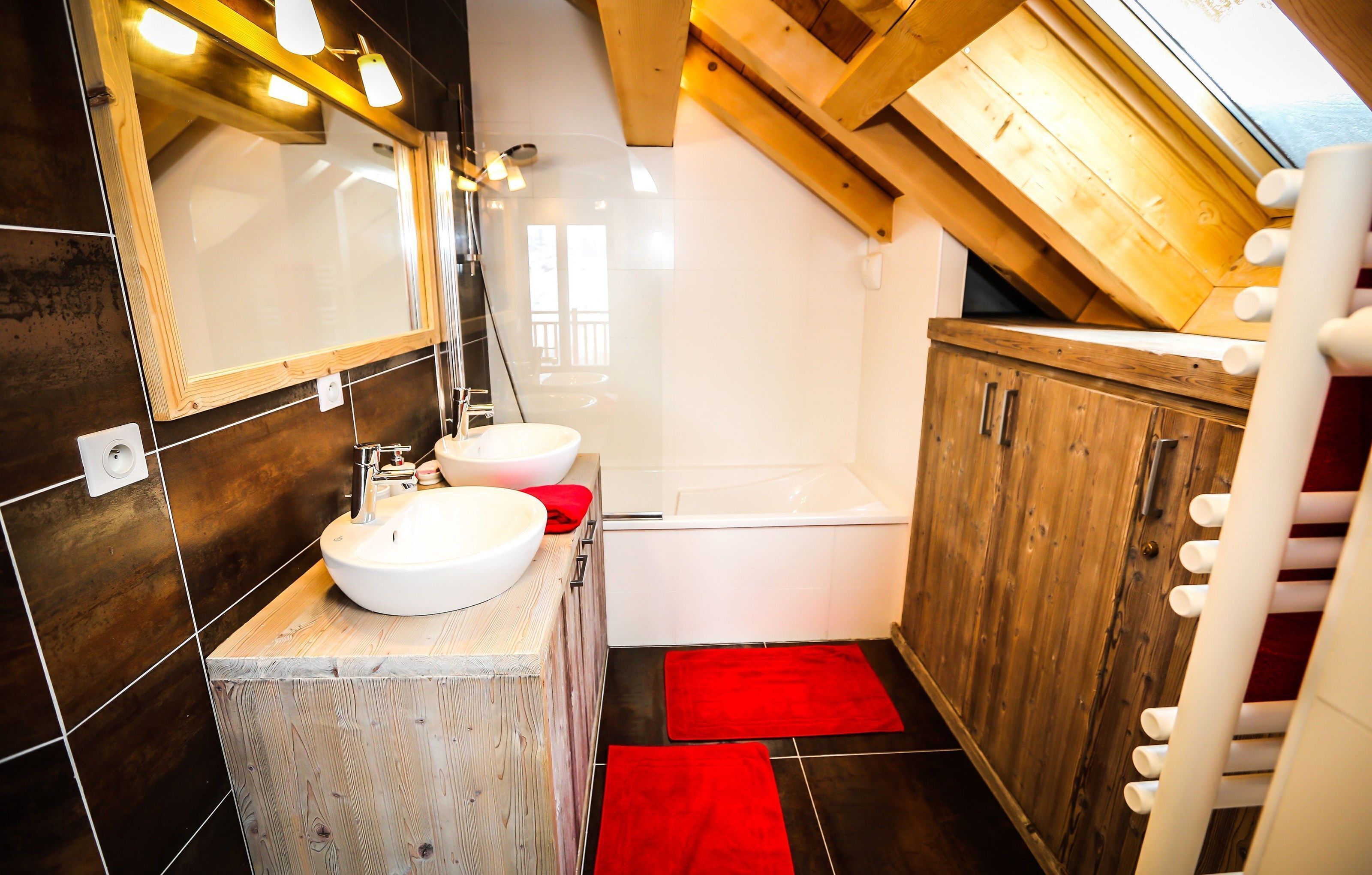 Een moderne badkamer met een houten wastafelmeubel, een grote spiegel, een bad en een rood vloerkleed.