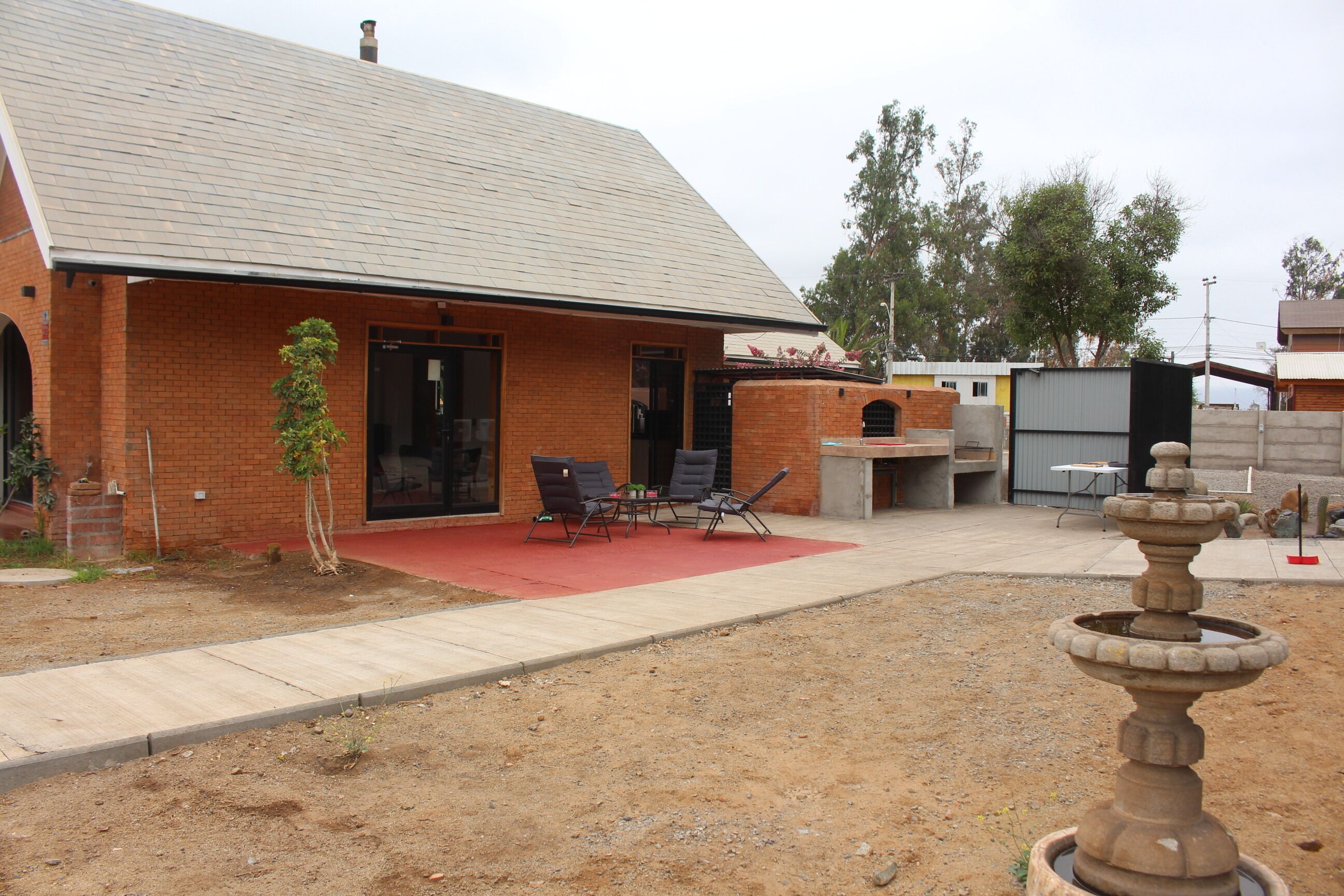 A brick building with a red roof, a patio with chairs, and a fountain.