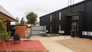 Un espace extérieur aménagé en terrasse, avec des sièges, un tapis rouge et un bâtiment à la façade noire.