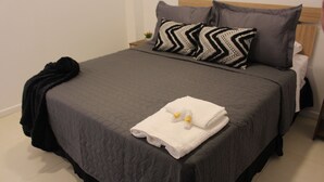 Un lit bien fait, avec une couette grise, un plaid noir et une serviette blanche accompagnée d’articles de toilette.