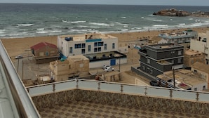 A coastal view with buildings near the beach, a checkered floor pattern, and a distant rocky outcrop. - CTM - Le Bateau (Terga)