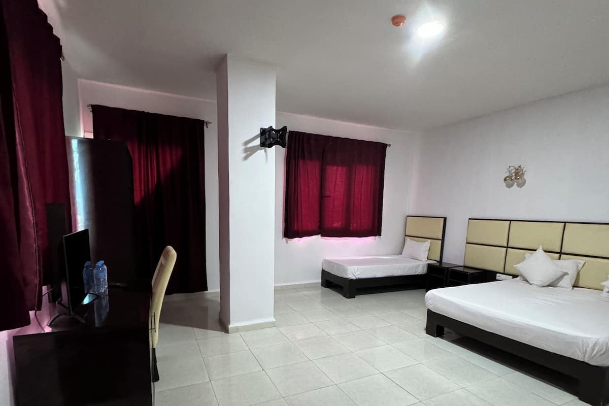A hotel room with a bed, a desk with a chair, a TV, and a window with curtains.