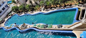 A large, winding pool with clear blue water, surrounded by palm trees and a white building. - CTM - Le Bateau (Terga)
