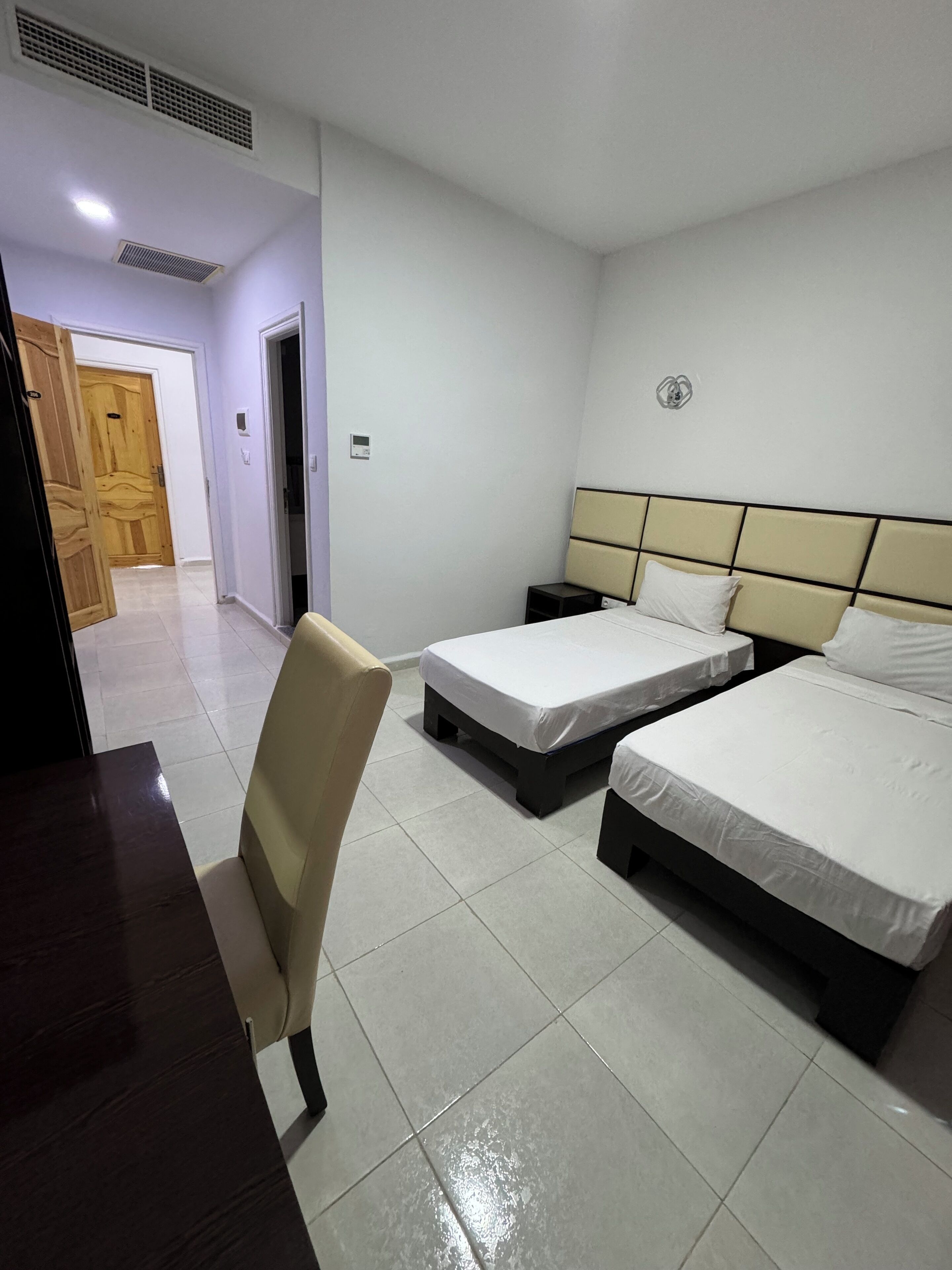 Habitació d'hotel amb dos llits, un escriptori, una cadira i una porta que dona a una altra habitació.