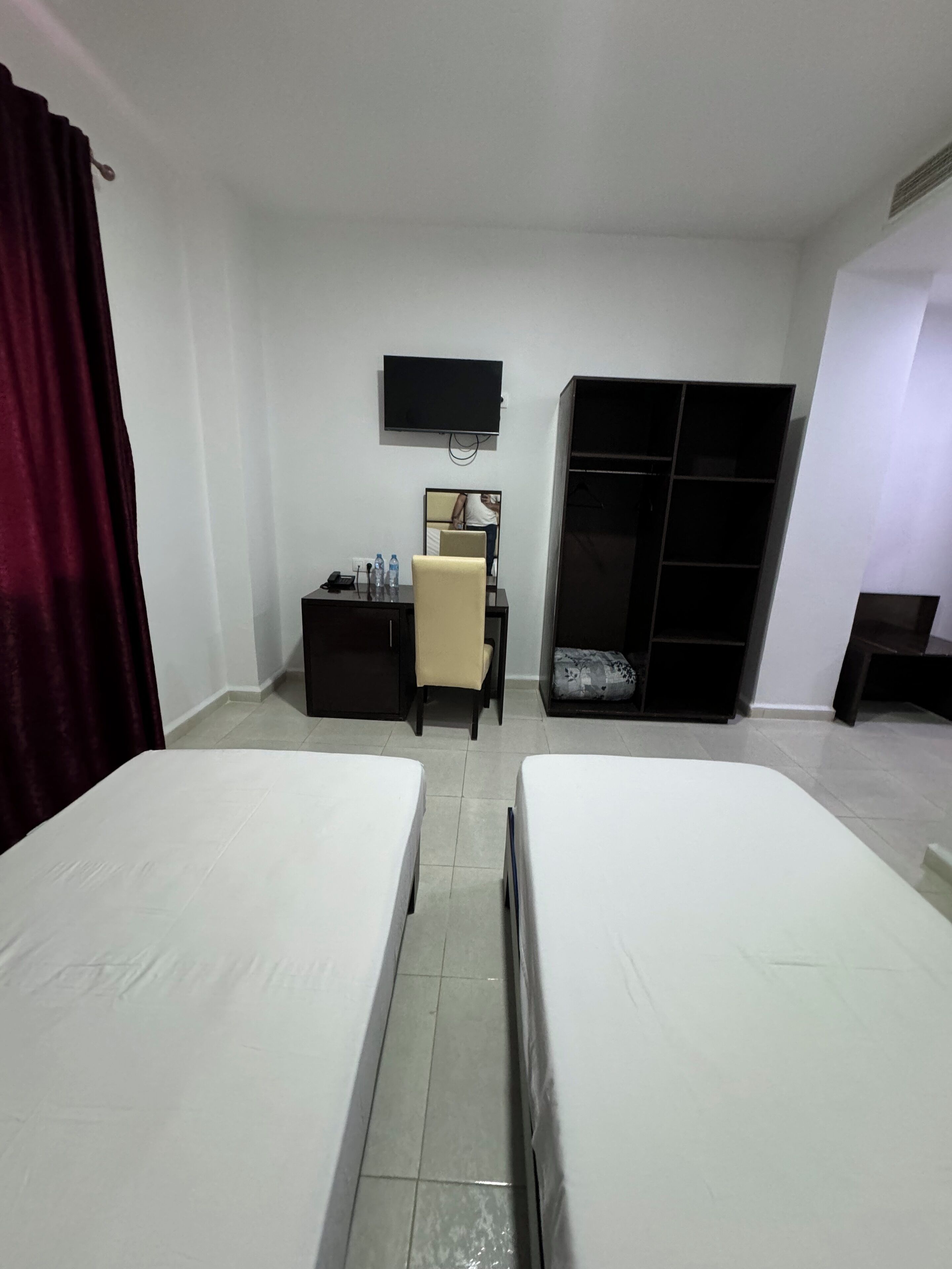 Habitación de hotel con dos camas, un escritorio con silla, televisor montado en la pared y un armario.
