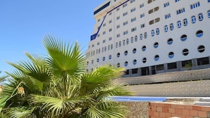 A multi-story hotel with a modern design, featuring a series of balconies and a prominent palm tree in the foreground. - CTM - Le Bateau (Terga)