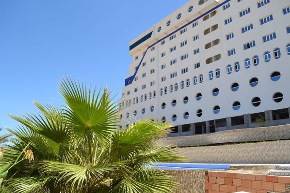Ein mehrstöckiges Hotel mit modernem Design, ausgestattet mit mehreren Balkonen und einer auffälligen Palme im Vordergrund.