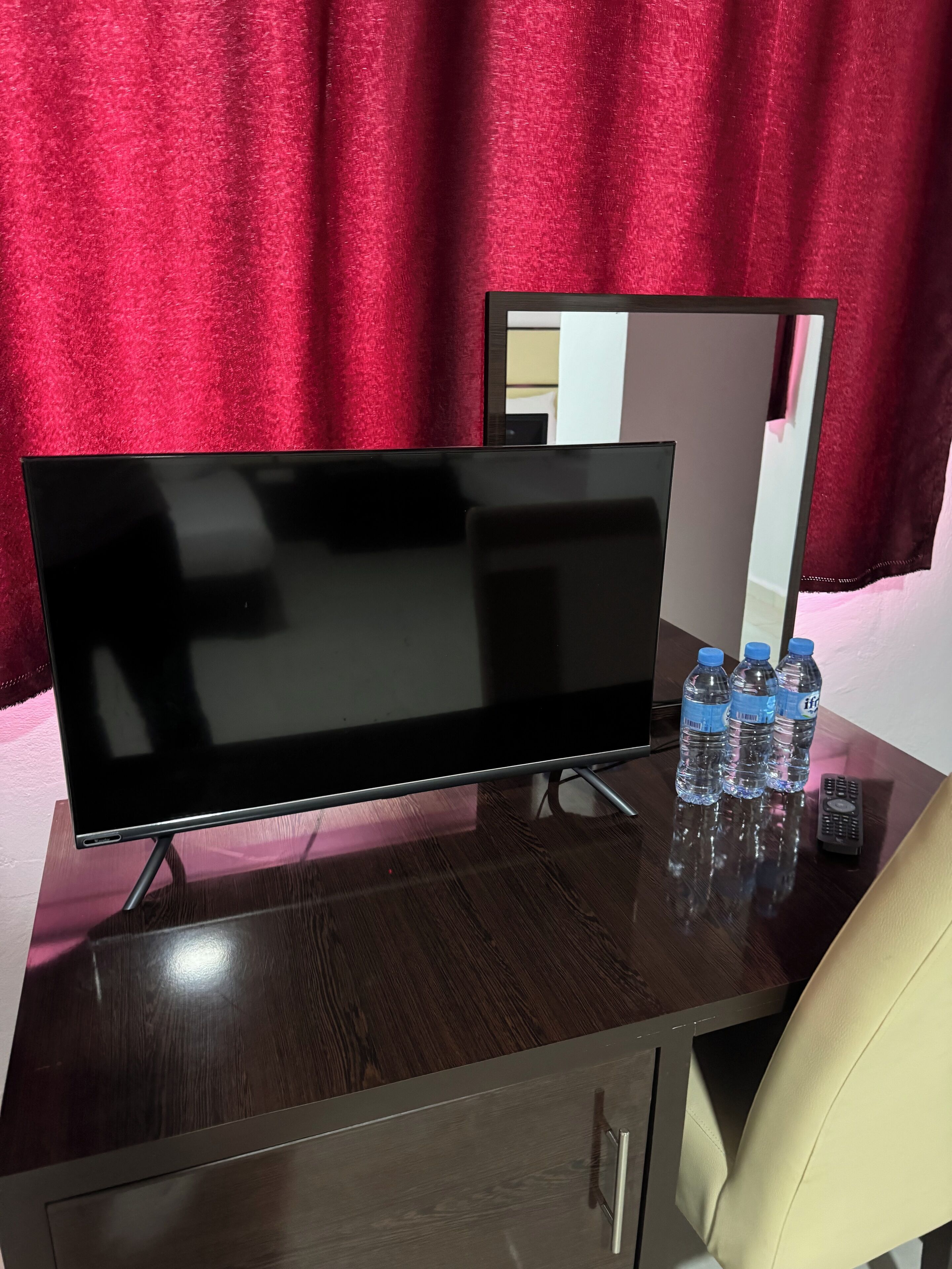 Een flatscreen televisie op een houten bureau met een spiegel, drie waterflessen en een afstandsbediening.