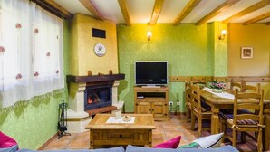 Ein gemütliches Wohnzimmer mit Kamin, Fernseher, Holzmöbeln und einem Essbereich.