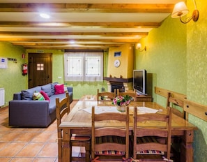 A cozy room with a wooden dining table, a sofa, and a television. - Casa Rural Balagar in Villablino, Laciana Valley with Pool (Caboalles De Abajo)