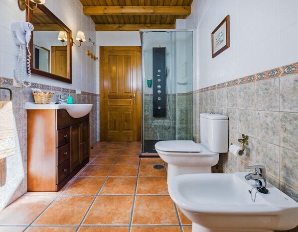 A bathroom with a wooden door, a shower, a sink, and a toilet.