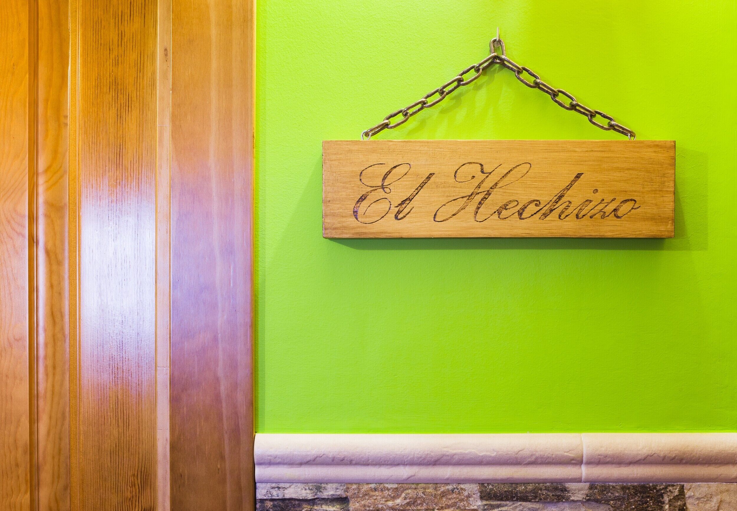 Un letrero de madera con 'El Helcho' sobre un muro verde.