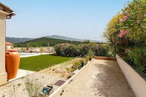 A garden with a pool, a large terracotta pot, and a view of hills.