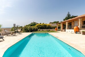 A rectangular swimming pool with a tiled deck, surrounded by outdoor furniture and potted plants.