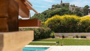 A pool area with a view of a hilltop building, surrounded by greenery and flowering plants.