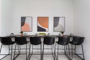 Een eetruimte met een lange tafel, zes zwarte stoelen en drie abstracte kunstwerken aan de muur.