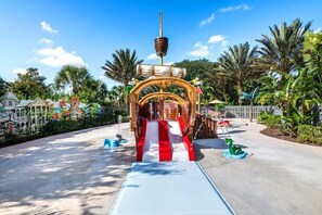 Un toboggan aquatique avec une arche en bois, des palmiers et un ciel dégagé.