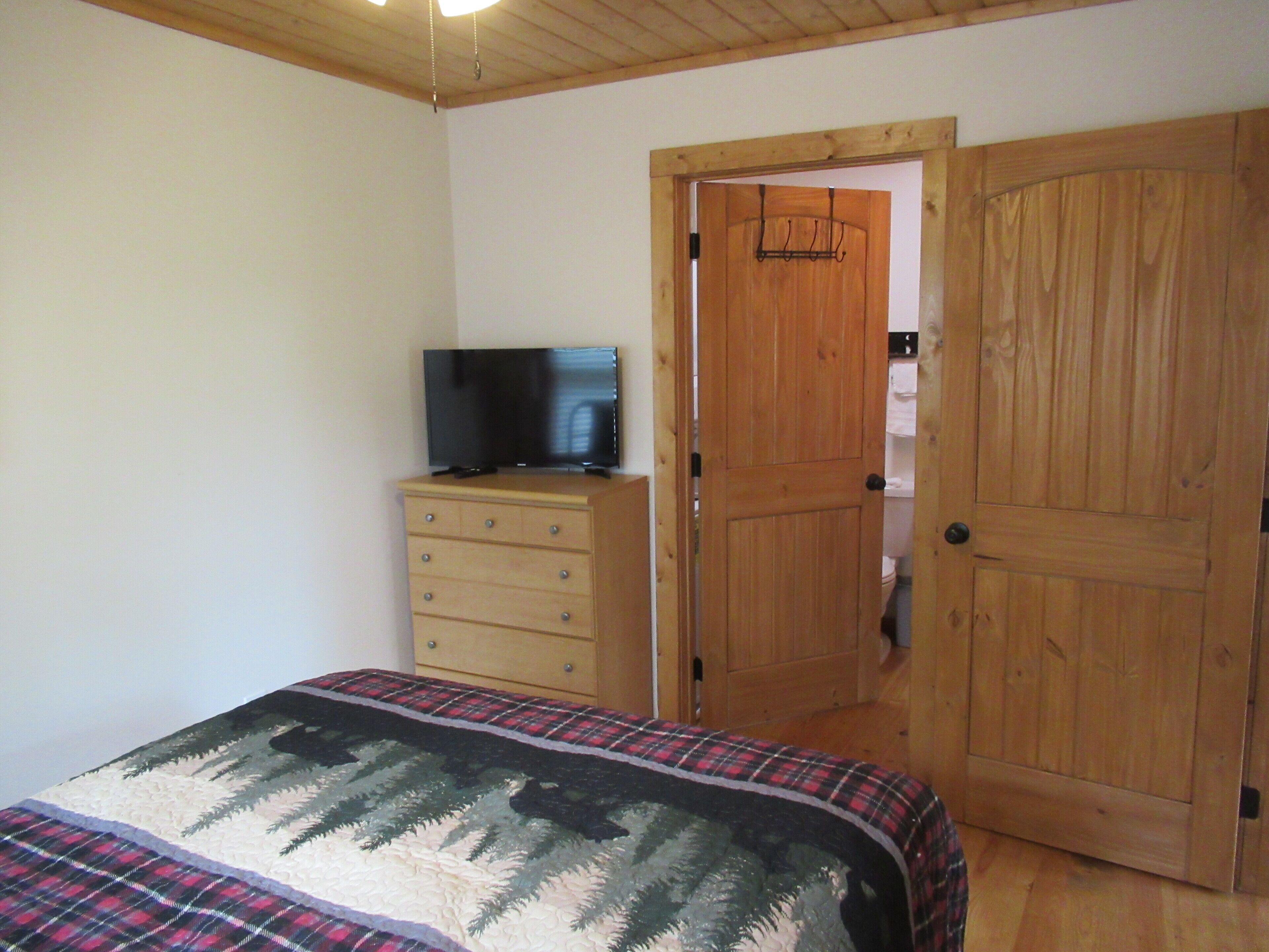 Ein Schlafzimmer mit einem Bett, einem Holzschrank, einem Fernseher und einer Holztür.
