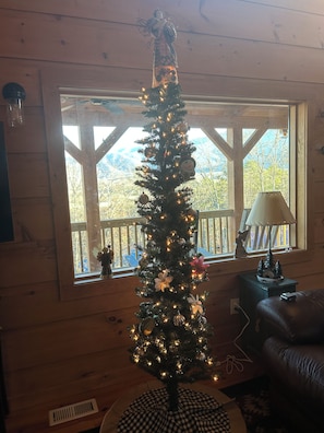 A Christmas tree with lights and ornaments in a room with wooden walls and a window overlooking a mountainous landscape.