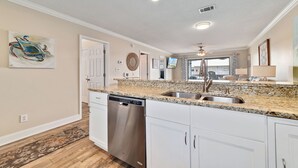 A kitchen with white cabinets, granite countertops, a stainless steel dishwasher, and a sink. - Bayview 70 w/Dock & Boat Slip | Dog Friendly | My Beach Getaways (Orange Beach)