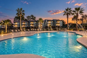 A swimming pool with lounge chairs and a water fountain, surrounded by multi-story buildings with balconies.
