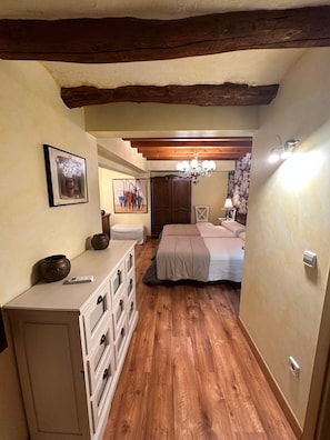 A bedroom with a wooden floor, a bed, a dresser, a cabinet, a chandelier, and a painting on the wall.