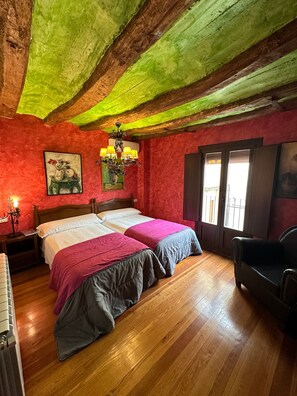 Une chambre avec deux lits, un lustre, un tableau et une fenêtre donnant sur un beau paysage.