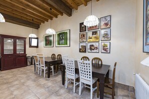 A dining area with a wooden ceiling, a dark wooden table, white chairs, and framed artwork on the wall.