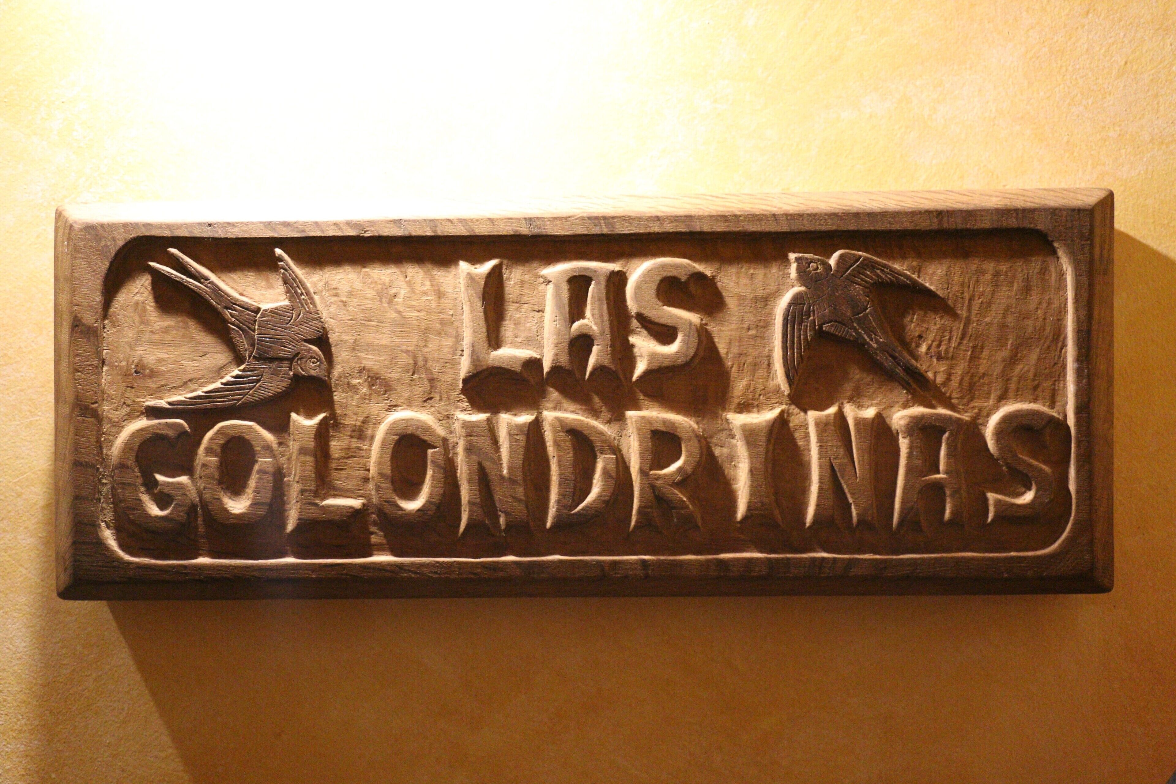 Une plaque en bois ornée d’oiseaux sculptés et portant l’inscription « LES GOLONDRIVAS ».