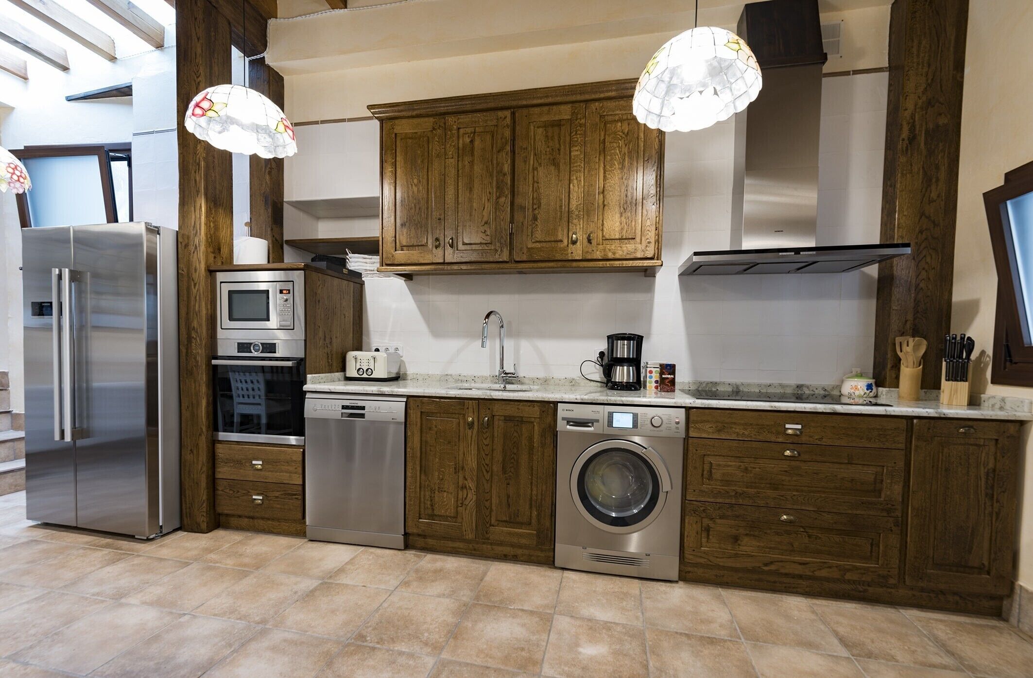 Une cuisine dotée de meubles en bois, d’appareils électroménagers en acier inoxydable, d’un lave-linge et de luminaires suspendus.