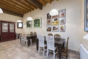 A dining area with a wooden ceiling, a dark wooden table, white chairs, and framed artwork on the wall.