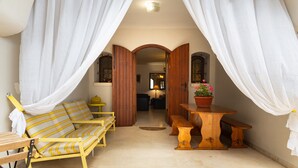 Ein Zimmer mit einem Bett, einer hölzernen Bank, einem kleinen Tisch mit einer Topfpflanze und einer Tür zu einem anderen Raum.