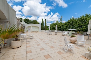 A spacious outdoor patio with tiled flooring, white chairs, and umbrellas.