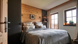 A bedroom with a wooden headboard, a bed with multiple pillows, a bedside shelf, and a window with a view. - Chalet Evi - TOP 1 (Kaprun)