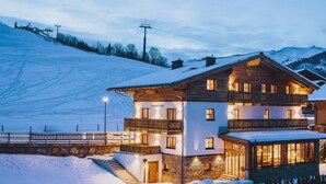 A two-story chalet with a balcony, a stone facade, and a ski lift in the background. - Chalet Evi - TOP 2 (Kaprun)