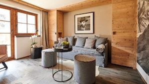 A cozy room with a wooden ceiling, a grey sofa, a round table with a vase, and a large framed picture on the wall. - Chalet Evi - TOP 2 (Kaprun)