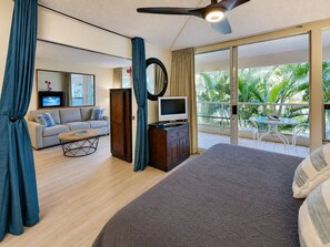 Una habitación de hotel con cama, sofá, televisión, escritorio y balcón con mesa y sillas.
